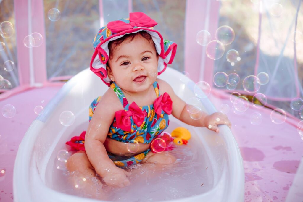 Smiling baby sitting in a small pink bathtub with bubbles