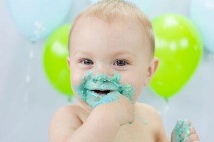 Laughing baby with a face covered in green frosting in front of balloons