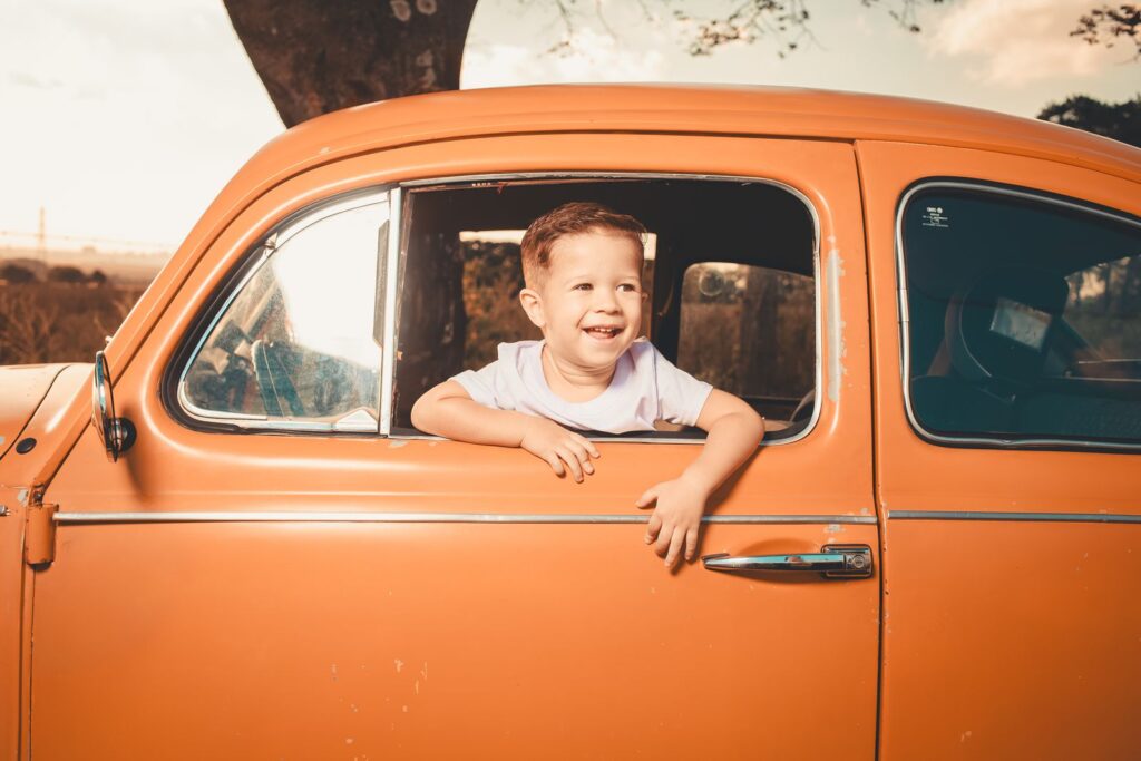 Smiling boy leaning out of the window of an orange car