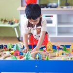 Boy playing at a colorful play table in a bright playroom with white shelves