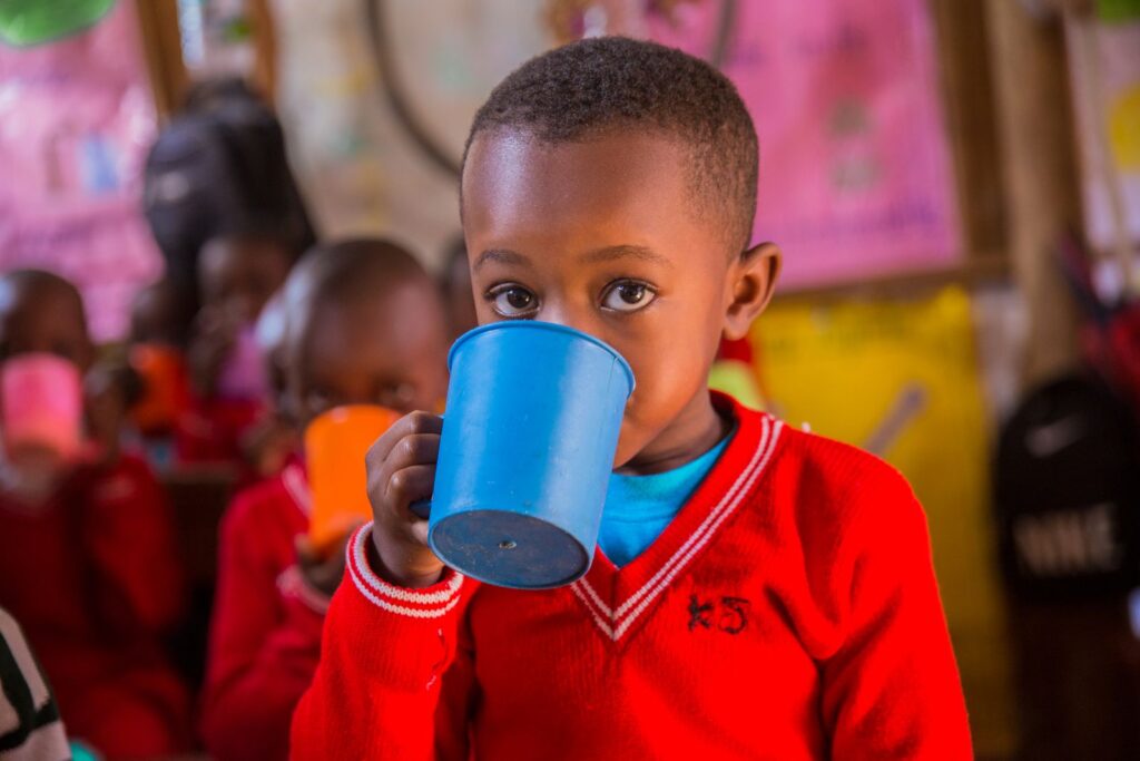Young boy in a red sweater drinking from a blue cup