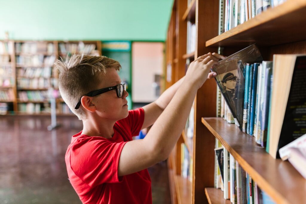 Boy reaching for a book on a library shelf