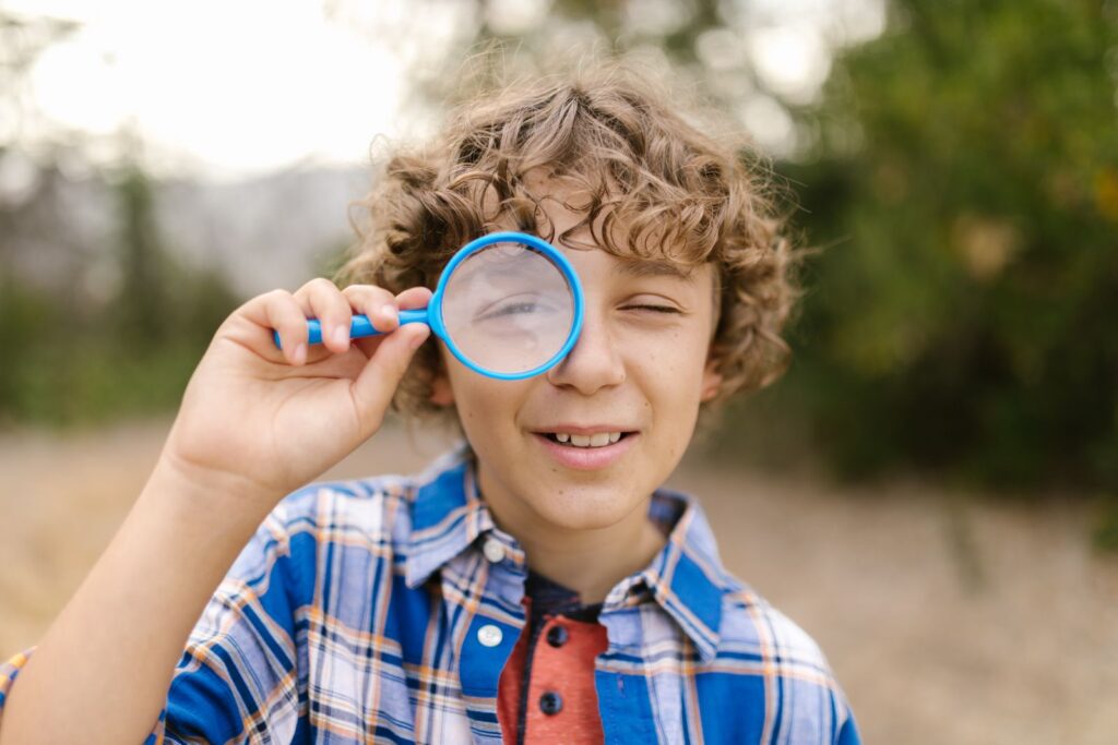 Smiling boy looking through a magnifying glass outdoors