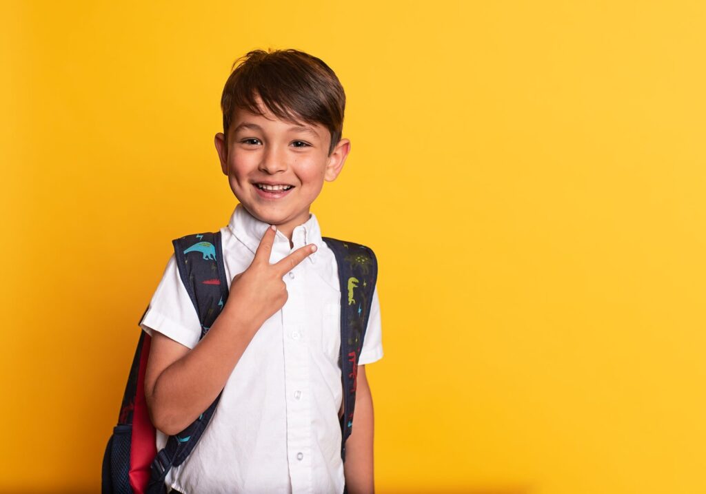Smiling boy wearing a school backpack against a yellow background