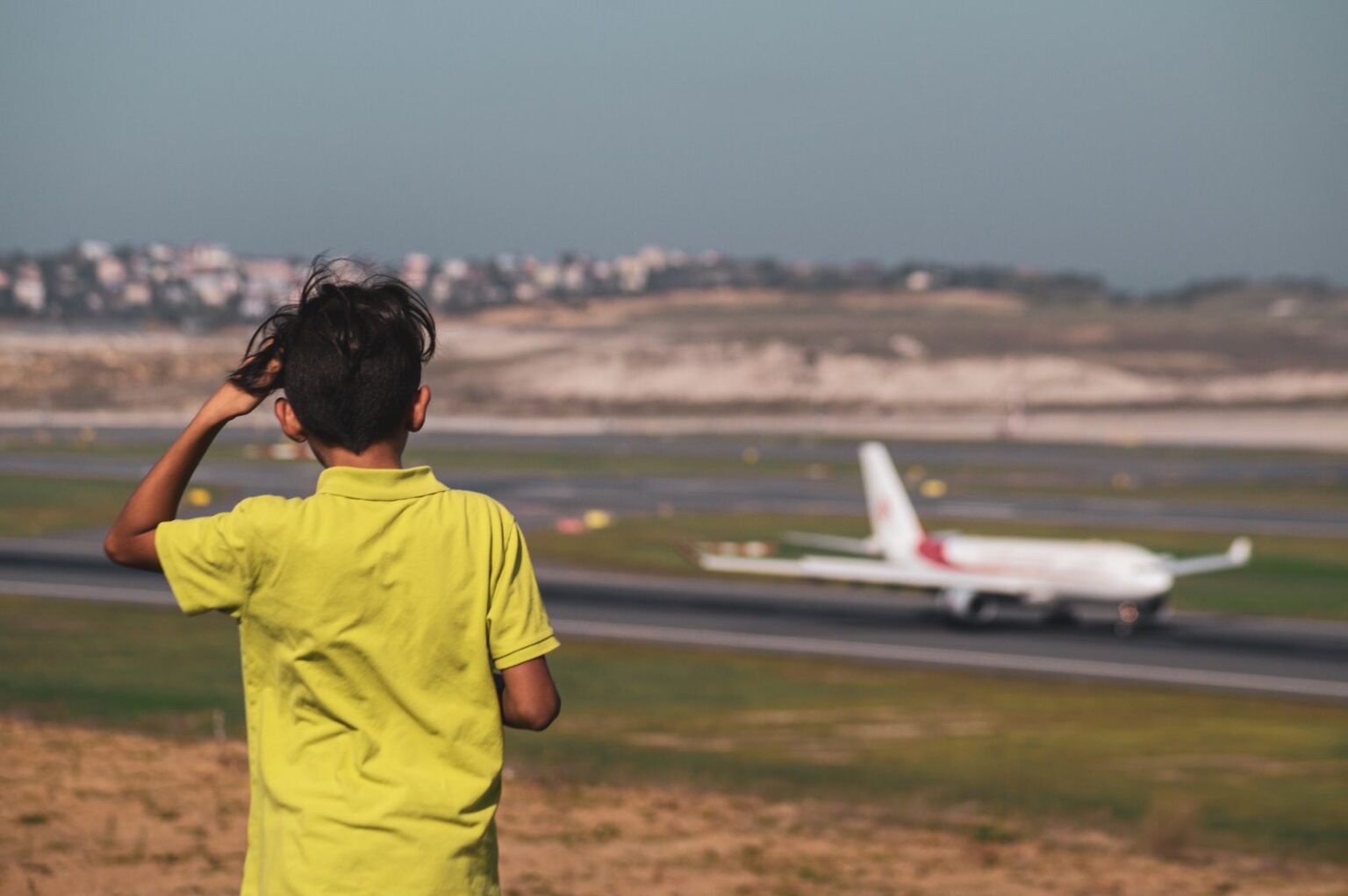 Boy in a yellow T-shirt watching a plane on the runway
