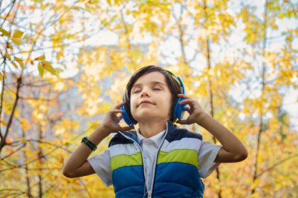Smiling boy listening to headphones with his eyes closed among yellow autumn leaves