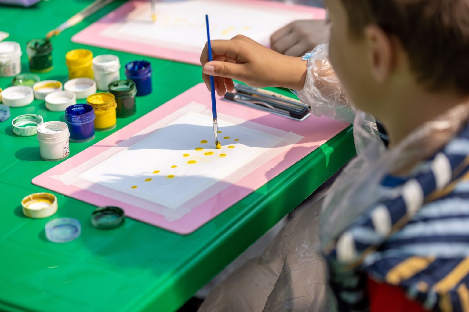 Child painting at a green table surrounded by pots of colorful paint