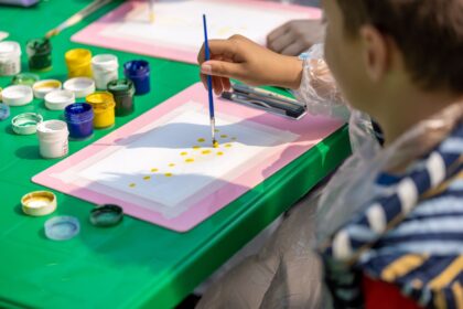 Child painting at a green table surrounded by pots of colorful paint