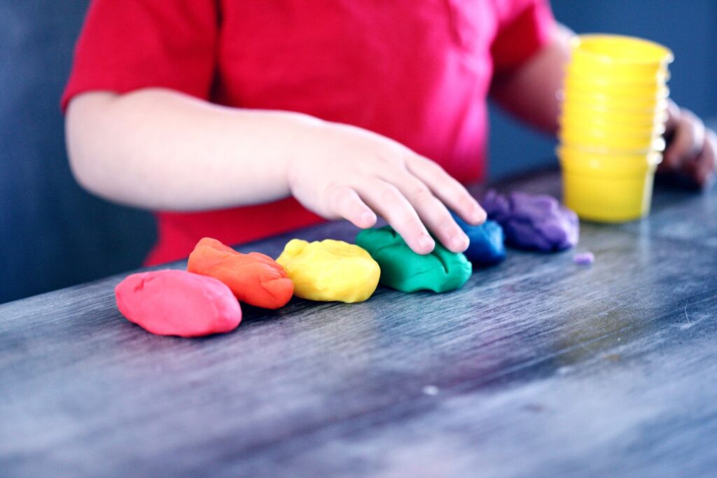 Child rolling bright balls of play dough on a table