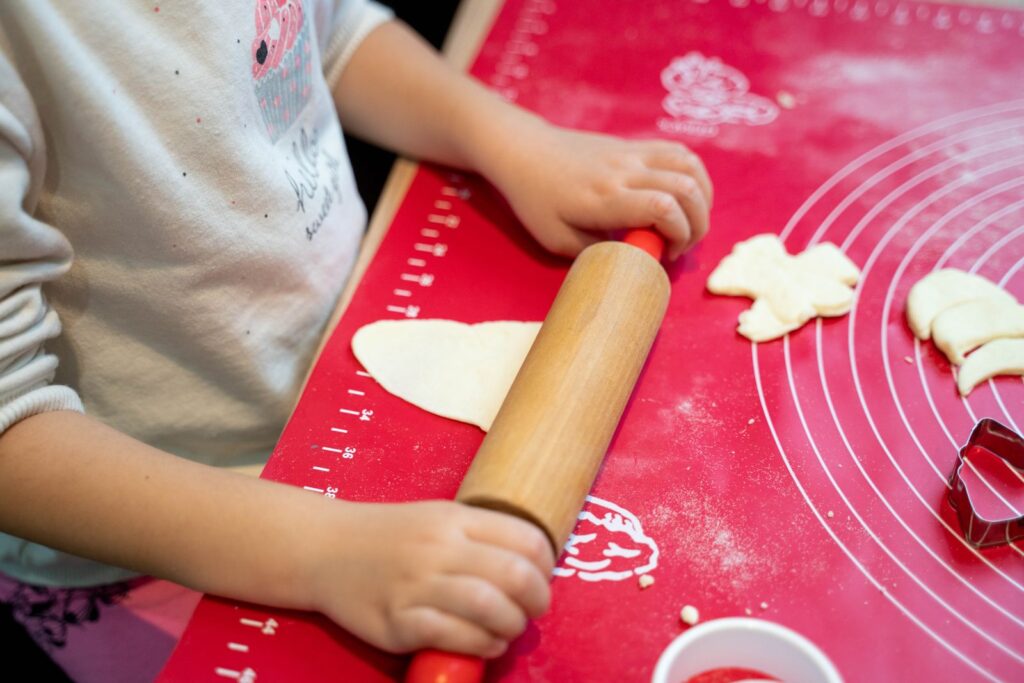 Child rolling cookie dough with a rolling pin on a red baking mat