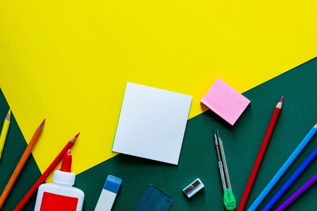 Colored pencils, glue stick and sticky notes on a yellow and green background