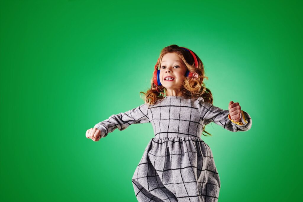 Girl in pink headphones dancing against a bright green background