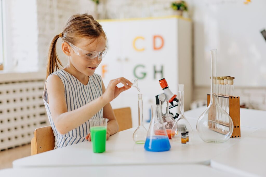 Girl in safety goggles doing an experiment with colorful test tubes