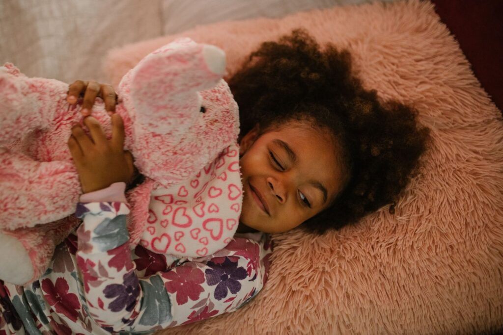 Young girl asleep hugging a soft pink toy on a fluffy blanket