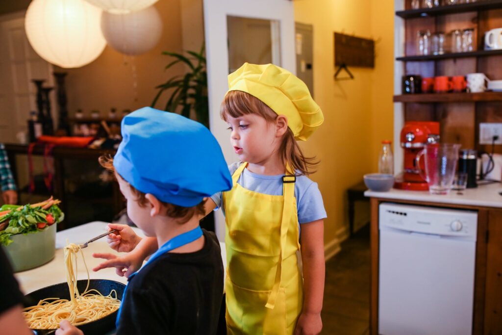 Two children in colorful chef hats and aprons cooking together
