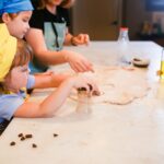 Children in chef hats and aprons rolling dough at a kitchen counter