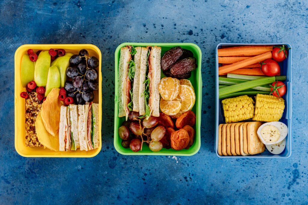 Three kids' lunch boxes packed with sandwiches, fruit, vegetables and crackers