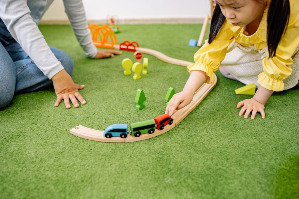 Children playing with a wooden train set on a green rug