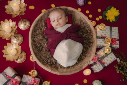 Newborn baby sleeping in a basket surrounded by colorful gift boxes