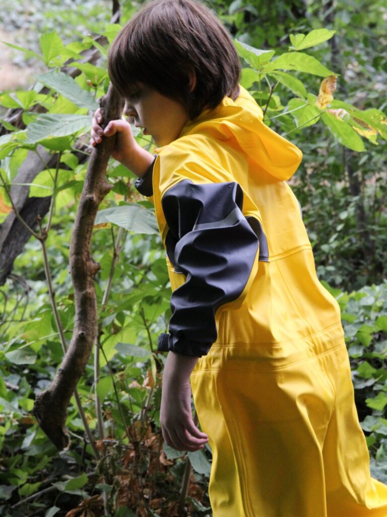 Child exploring outdoors in a bright yellow Oaki rubber rain suit