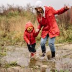 Parent and child in red coats jumping in a muddy puddle together