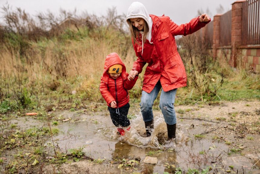 Parent and child in red coats jumping in a muddy puddle together