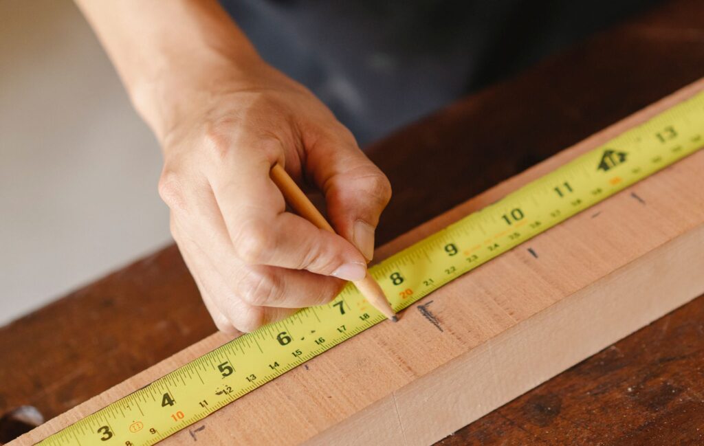 Hand marking a measurement on a wooden board with a tape measure