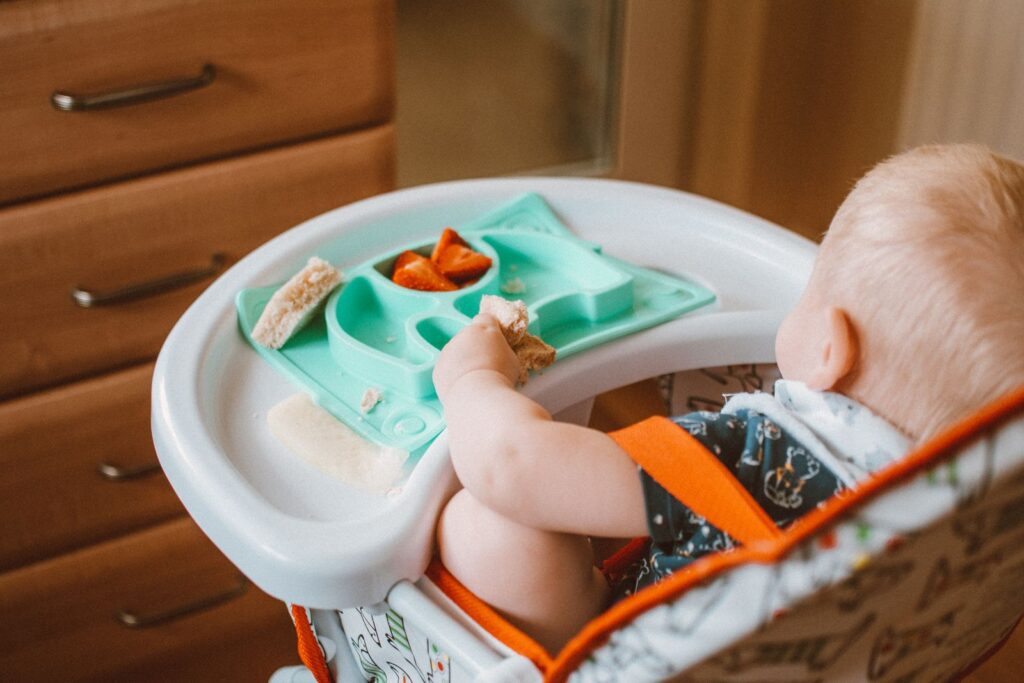 Toddler in a high chair eating from a teal divided suction plate