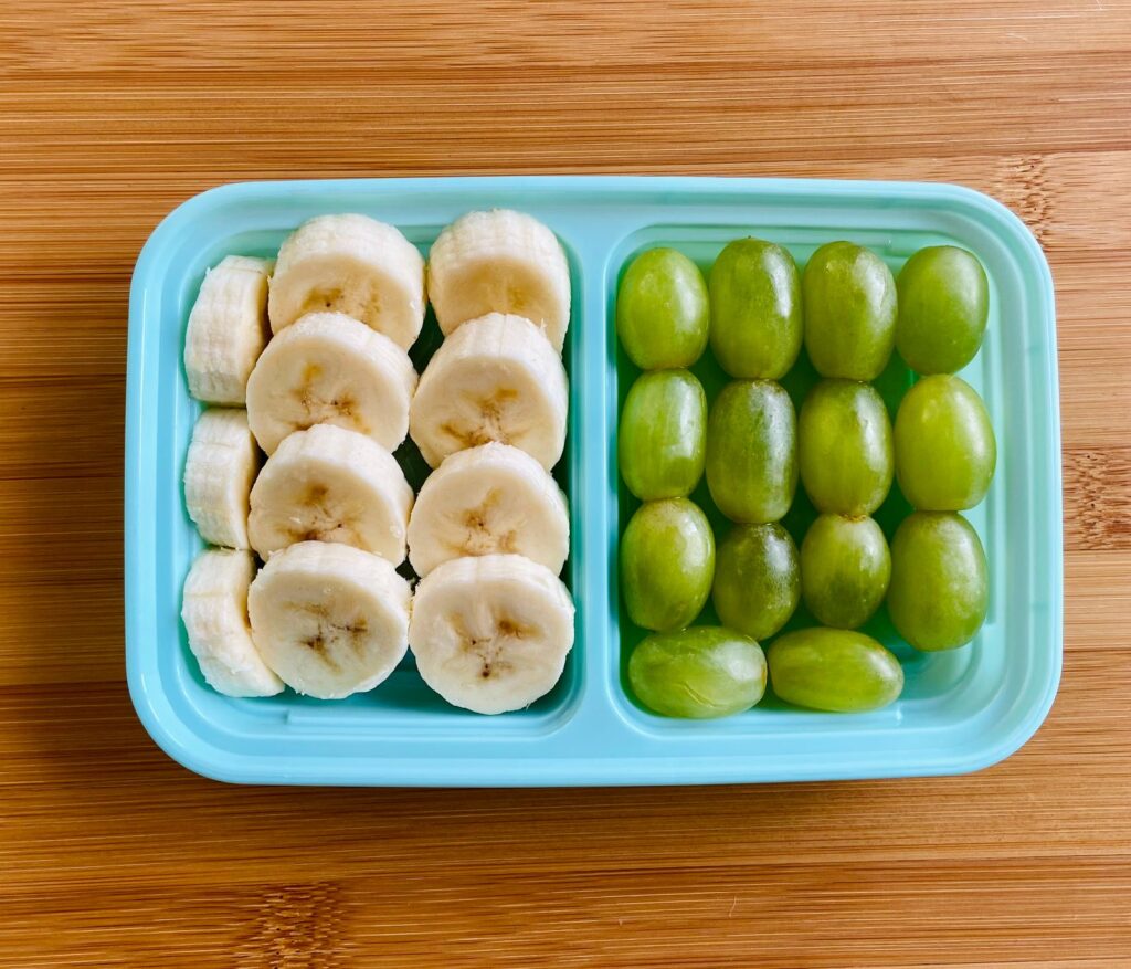 Banana slices and green grapes in a teal snack container
