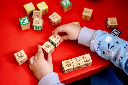 Toddler arranging wooden alphabet blocks on a bright red table