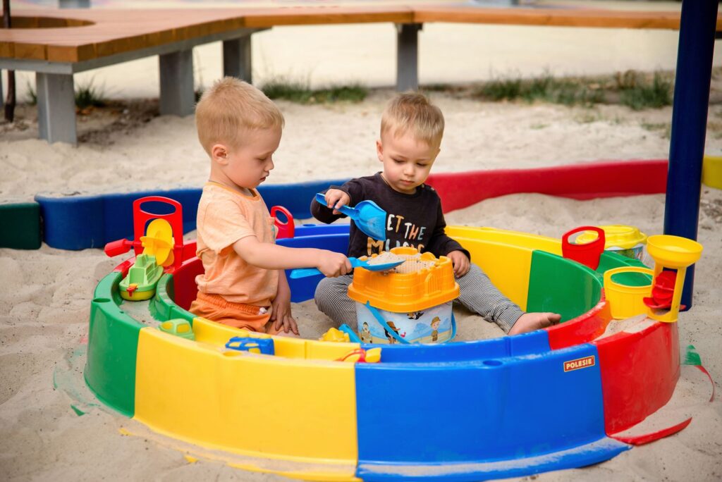 Two toddlers playing in a bright plastic sandbox